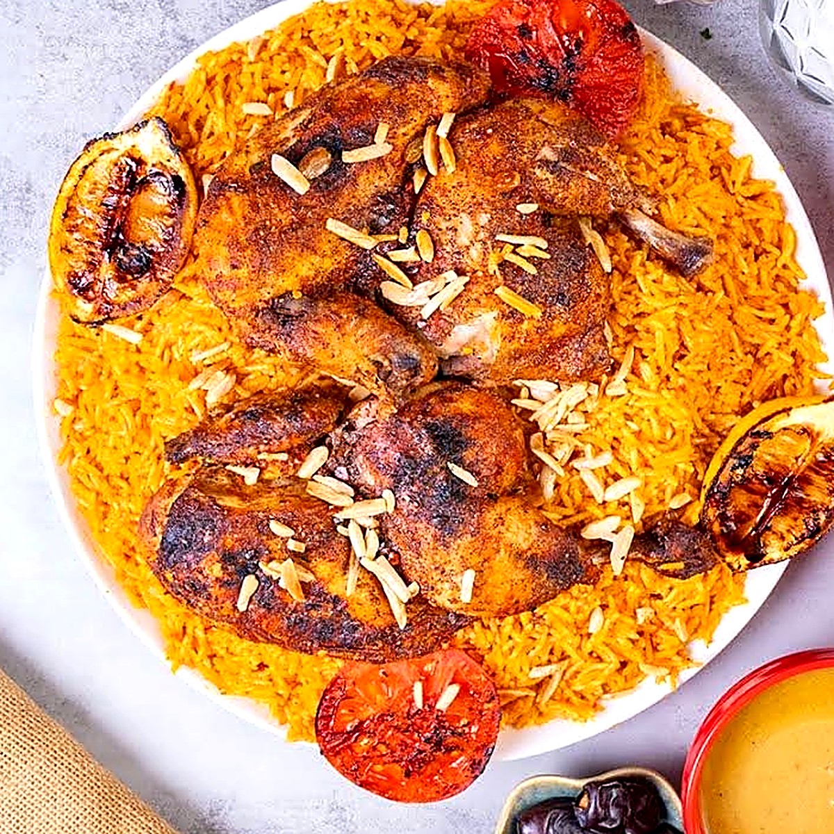 Two grilled chickens over spiced rice with almonds and charred tomato