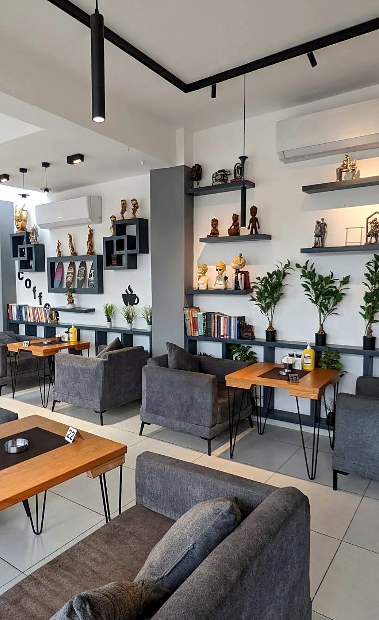 Grey armchairs and wooden tables beside shelves of books and small objects