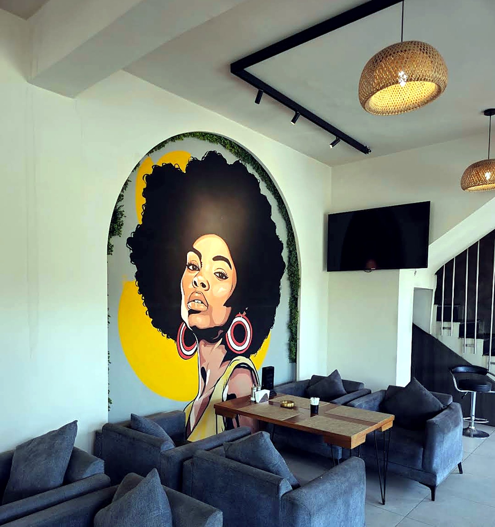 A framed portrait mural above a corner of grey armchairs and a wooden table