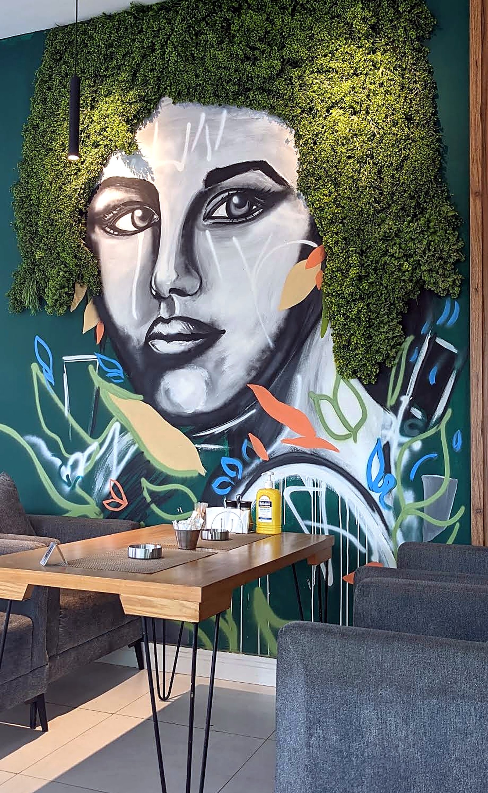 A large painted portrait mural with foliage hair on a deep green wall